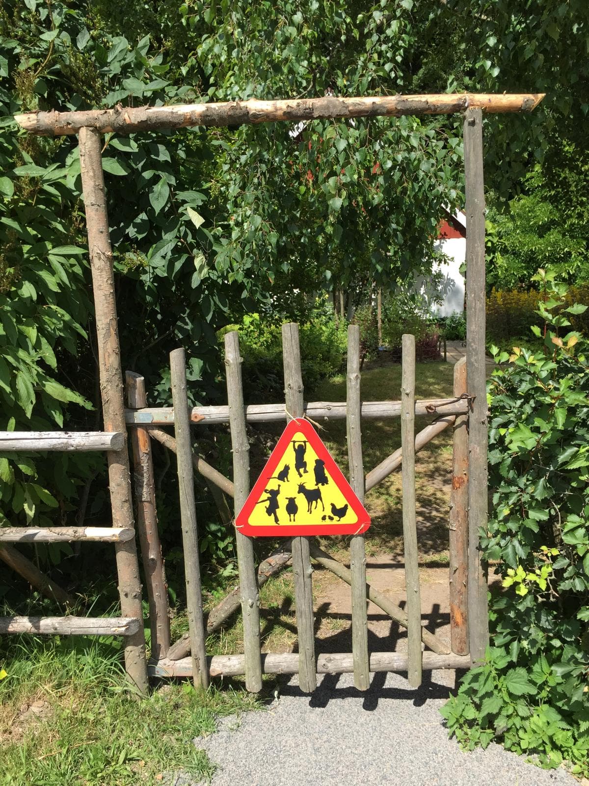 Varningsskylt på grinden till trädgården som skämtsamt varnar för lekande barn och olika djur.