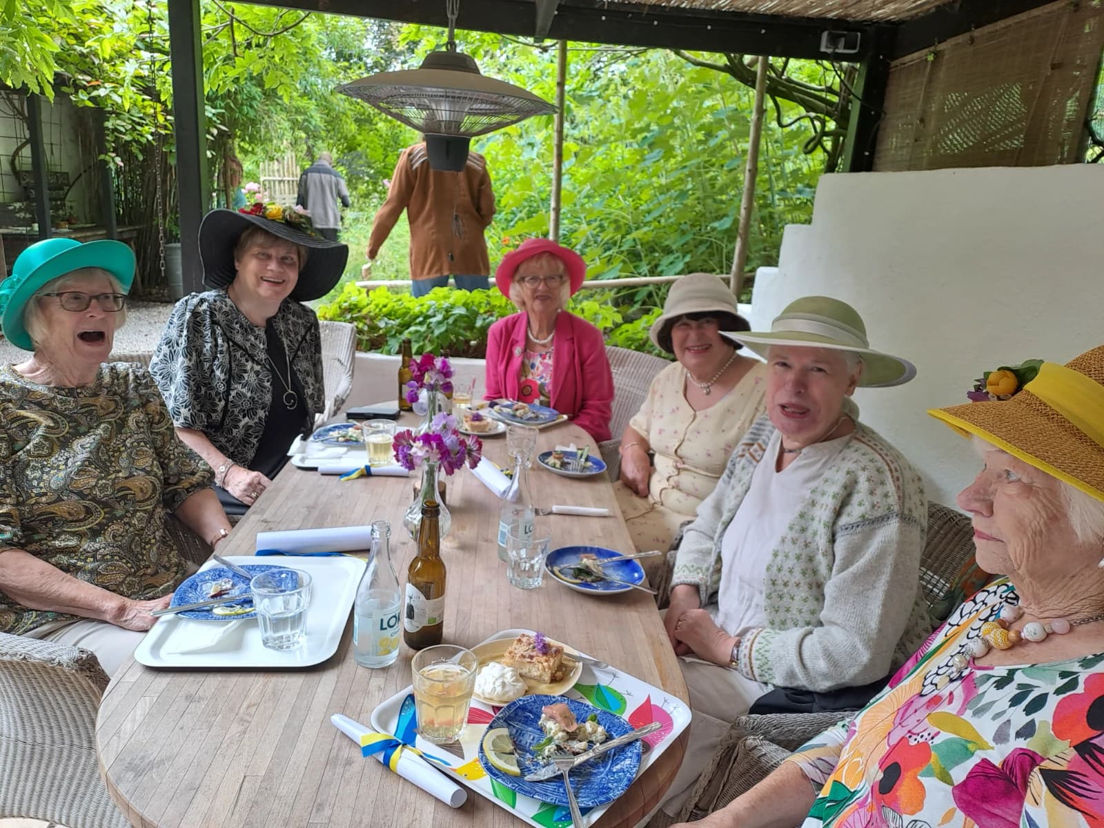 Grupp av glada damer i hatt äter lunch vid uteserveringen
